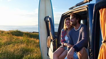 A couple in travel van smiling outdoors 