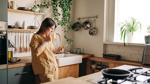 Woman leaning on sink drinking orange juice looking down her phone