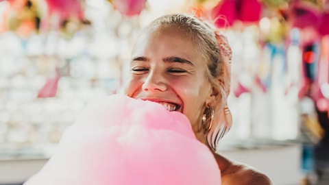 A woman in outdoor festival smiling with a big cotton candy stick