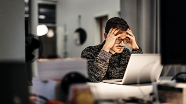 Man with a laptop open with his hands in his head looking stressed 
