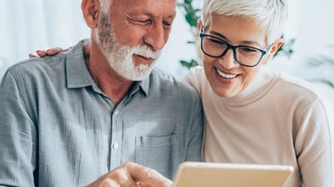 Older woman and man smile as they look over at device