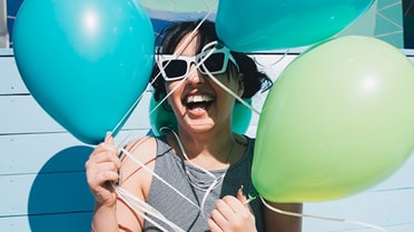 Woman in white sunglasses holding aqua and green balloons happy 