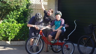 two kids hopping on a bike and a mother smiling 