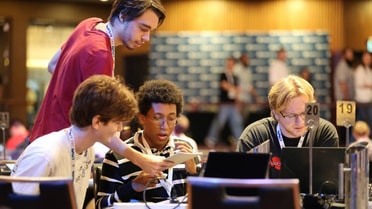 Hackathon - UoN Students gathered on a desk solving problems on their laptop and paper 