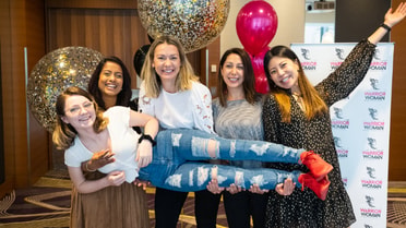 Four women hold one woman up while smiling 