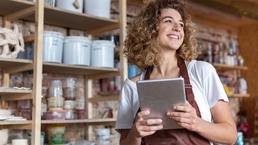 business owner in smock smiling in workshop holding a tablet device