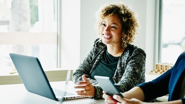 woman has a laptop opening communicating with another person across the table