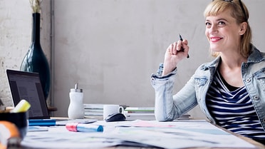 Woman looks up smiling holding a pen in hand 