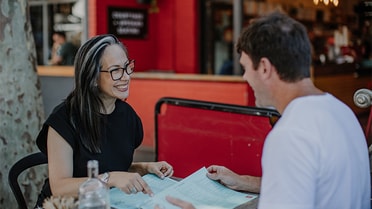 Woman and man smile as they're looking through menus in outdoor restaurant 