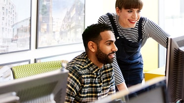 Woman helps a man while he's on the computer smiling 