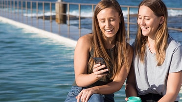pair sitting at Newcastle Ocean Baths smiling at phone