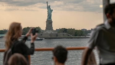Woman taking a photo of the statue of liberty in the distance