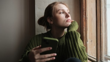 Girl in green jumper on mobile phone looking out window