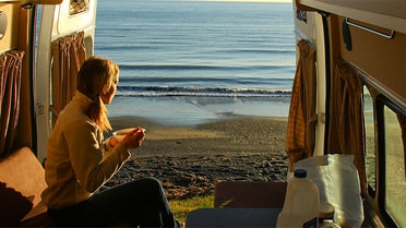 Van open to beach view with a man looking outside during sunset 