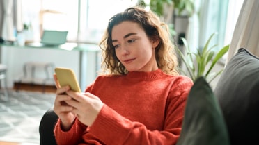 woman in natural themed home smiling at her phone 
