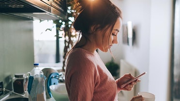 Woman in the kitchen holding a cup looking down on her phone