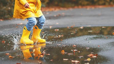 kid jumping in puddle with yellow raincoat and boots on