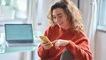 Woman confusingly smiles at her phone on her desk 