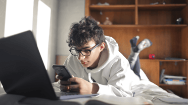 Teenage boy on his phone with his laptop open