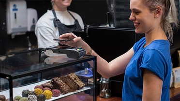 Woman tapping her phone on pay machine in a cafe 