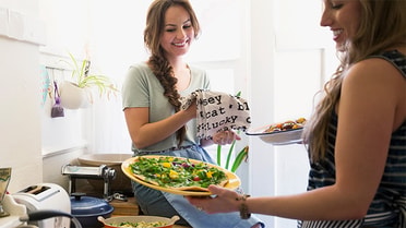Woman holding food bowls to another woman smiling 