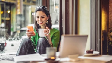 Woman in coffee shop on phone with laptop