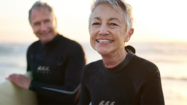older couple carrying surfboards on beach