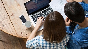 Pair on laptop holding paperwork