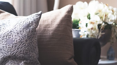 decorative cushions on a couch with a vase of flowers on a table beside