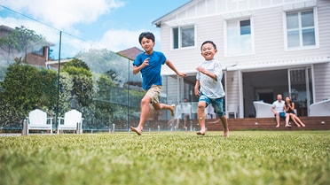 2 kids running across backyard as parents watch and smile