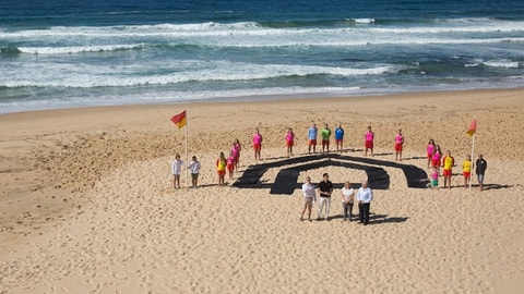 Newcastle Permanent employees and volunteers gathering in the beach with Newcastle Permanent black layout on sand
