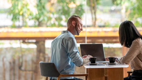 A woman and a man at a cafe sitting down looking at a laptop